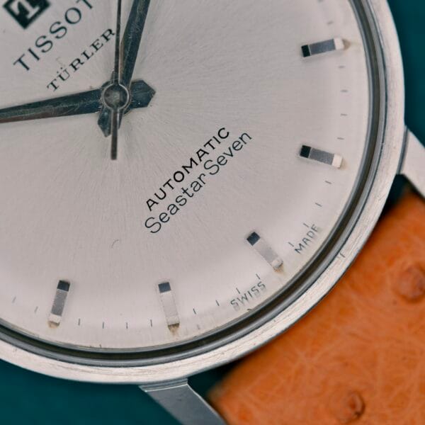 Close-up of a Tissot Automatic Seastar Seven Turler watch face, featuring a tan leather strap and silver details.