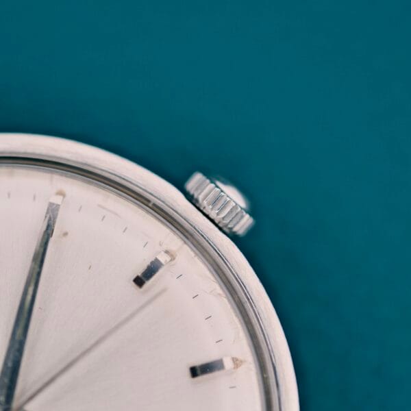 Close-up of the Tissot Automatic Seastar Seven Turlers silver crown and partial dial, set against a teal background.