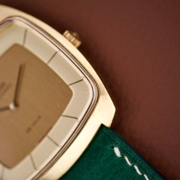 Close-up of an Omega Deville 151.0051 TV Case gold watch with a green leather strap, resting on a brown surface.