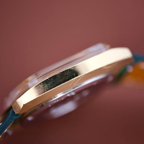 Close-up side view of an Omega Deville 151.0051 TV Case featuring a gold-colored finish, visible scratches, and paired with a blue strap.