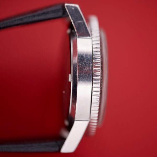 Side view of a Caravelle Worldtimer Ref. 753 Day/Date wristwatch with black strap, displayed on a solid red background.