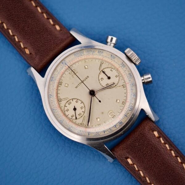 The Wittnauer Chronograph Venus 188 features the acclaimed Venus 188 movement and comes with a brown leather strap, showcased on a blue textured background.