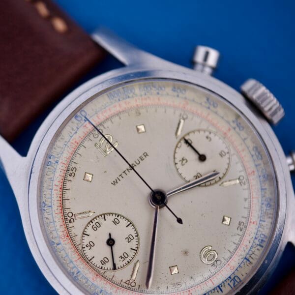Close-up of a Wittnauer Chronograph Venus 188 on a brown leather strap, displayed against a blue background.