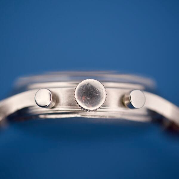 Close-up side view of the Wittnauer Chronograph Venus 188’s silver crown and pushers with the Venus 188 movement, set against a blue background.