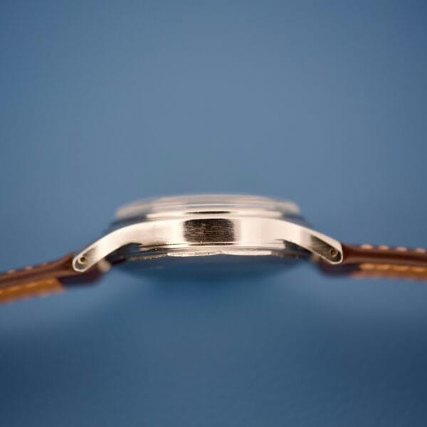 Side view of the Wittnauer Chronograph Venus 188 with a silver case, brown leather strap, and the famous Venus 188 movement, displayed against a blue background.