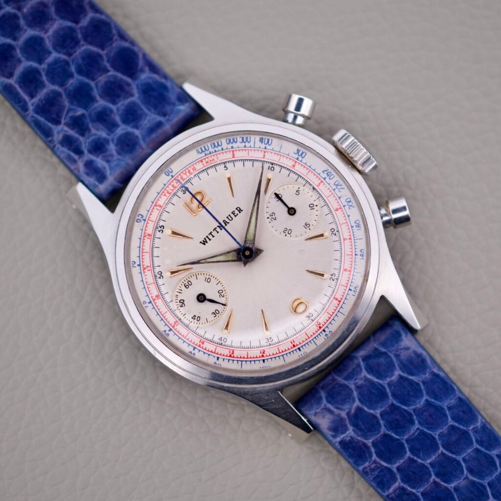 A Wittnauer 3256 Chronograph Venus 188 watch with a blue strap rests on a textured gray surface.