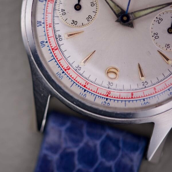 Close-up of a Wittnauer 3256 Chronograph Venus 188 wristwatch with a blue strap, white dial, gold markers, and red-blue scales.