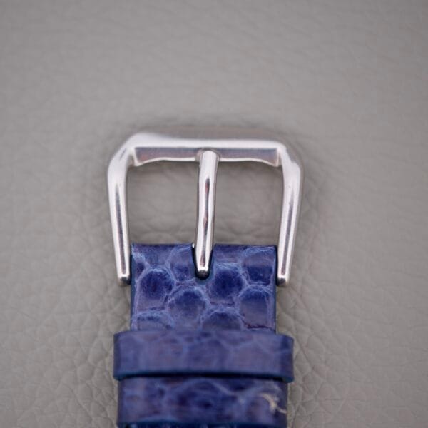 Close-up of a silver watch buckle on a textured blue leather strap from the Wittnauer 3256 Chronograph Venus 188, set against a light gray background.