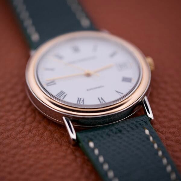 Close-up of a Girard Perregaux Automatic 4797 wristwatch featuring a white dial with Roman numerals, automatic movement, and a dark green leather strap on brown leather.