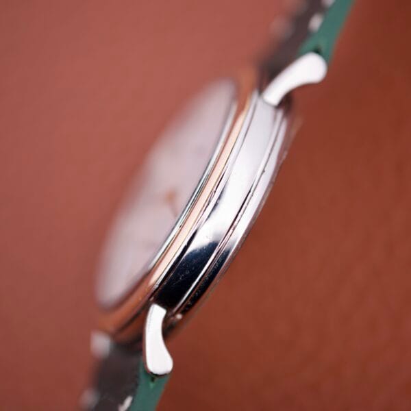 Close-up side view of the Girard Perregaux Automatic 4797 wristwatch in silver, featuring a green strap and set against a brown textured background.