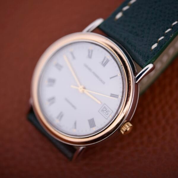 Close-up of the Girard Perregaux Automatic 4797 wristwatch, featuring a white face, gold trim, black leather strap, and date display.