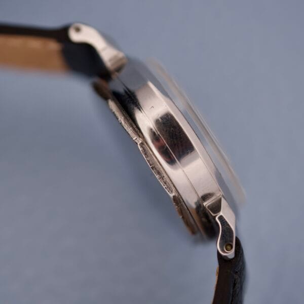Side view of a Tiffany & Co. By Movado 11729 wristwatch with a silver case and black leather strap, set against a light blue background.