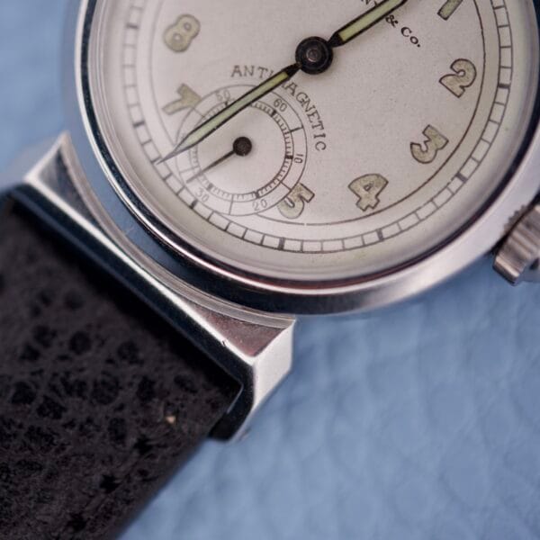 Close-up of a Tiffany & Co. By Movado 11729 vintage wristwatch with a black leather strap on a light blue textured surface.