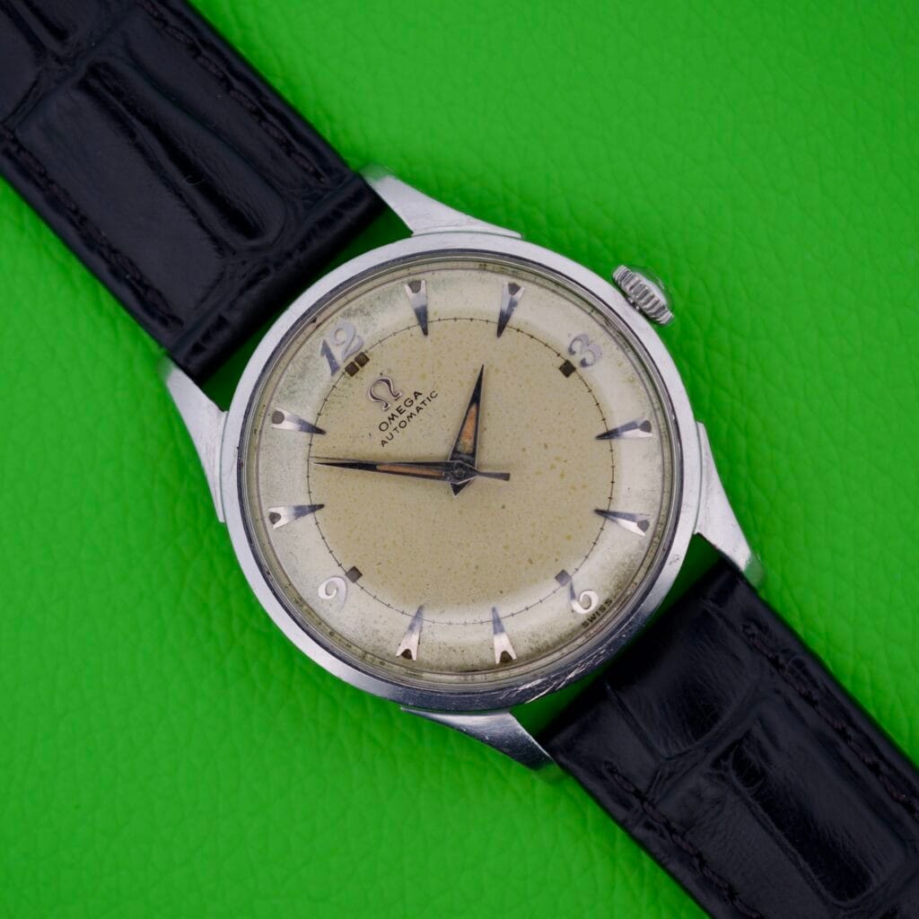 Omega Automatic Bumper 2635 Original Strap wristwatch with black leather band, displayed on a bright green textured background.
