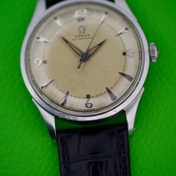 Omega Automatic Bumper 2635 wristwatch with a worn dial and original black strap, featured against a vivid green background.