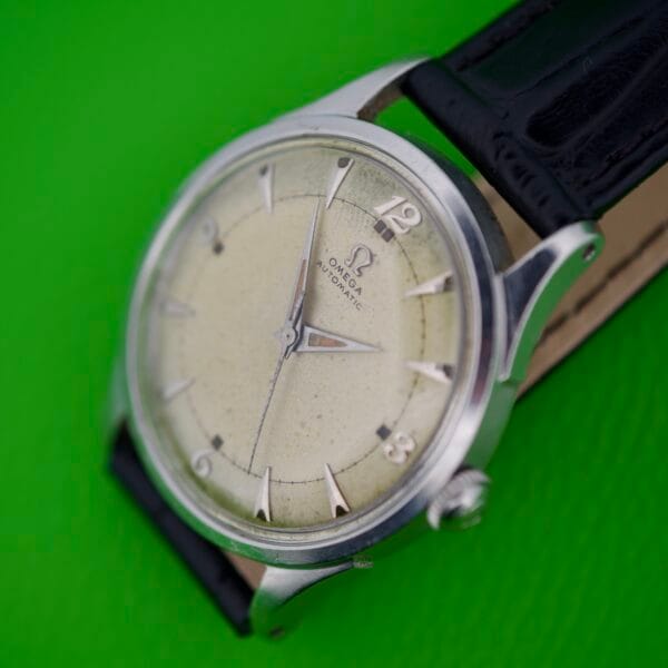 An Omega Automatic Bumper 2635 Original Strap wristwatch with a cream dial is displayed on a vibrant green background.
