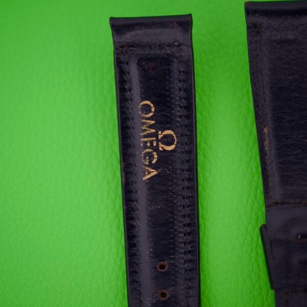 Close-up of the Omega Automatic Bumper 2635 Original Strap in black, with gold text displayed on a vibrant green textured background.
