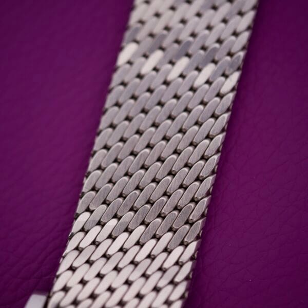 Close-up of a Movado Automatic 431 Stainless Steel watch band with mesh pattern, elegantly displayed on a textured purple surface.