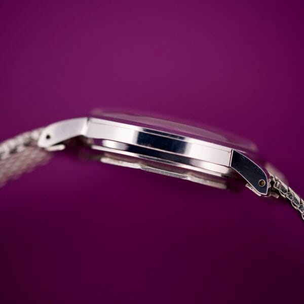 Close-up side view of the Movado Automatic 431 Stainless Steel wristwatch with a silver band, displayed against a purple background.