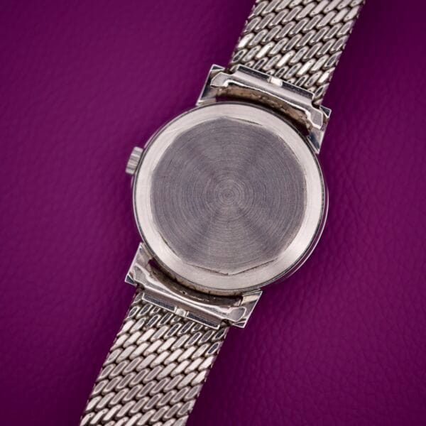 The Movado Automatic 431 Stainless Steel wristwatch with a mesh strap is shown face-down on a textured purple surface.