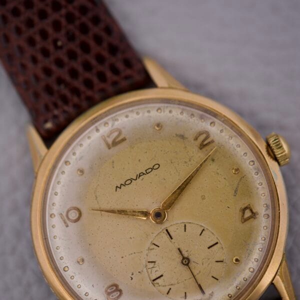 Close-up of a vintage Movado Jumbo Manual Wind Sub Seconds watch featuring a gold case, brown textured strap, aged speckled dial, and elegant sub seconds display.