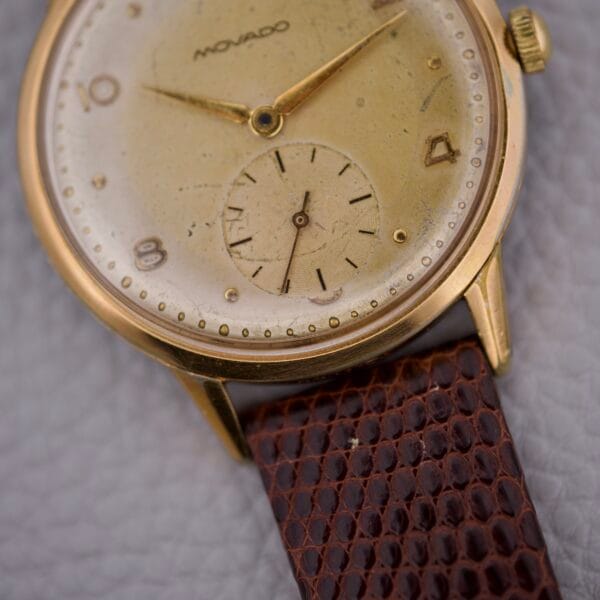 Close-up of a Movado Jumbo Manual Wind Sub Seconds gold wristwatch featuring a brown textured leather strap.