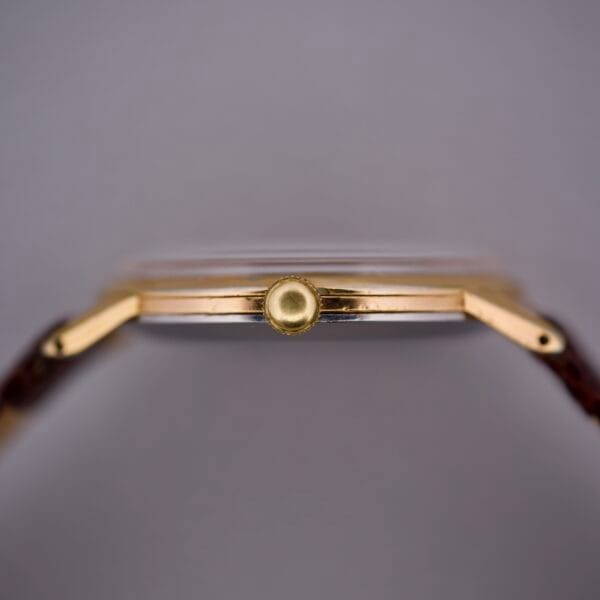 Close-up side view of the Movado Jumbo Manual Wind Sub Seconds gold wristwatch with a brown strap, highlighting the crown, slim case, and classic manual wind movement featuring a subsidiary seconds display.