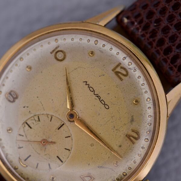 Close-up of a Movado Jumbo Manual Wind Sub Seconds wristwatch featuring a gold case, worn dial, and brown leather strap.