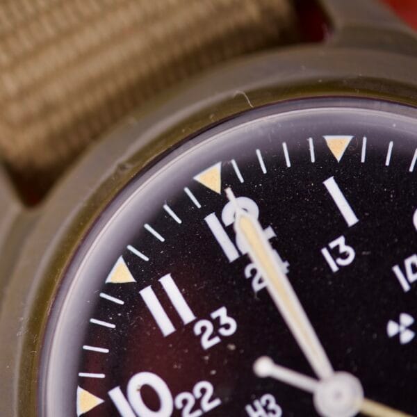 Close-up of the Benrus Mil-W-46374A US Military 1975 watch at 12:00, featuring a black dial and beige strap, inspired by the classic military spec.