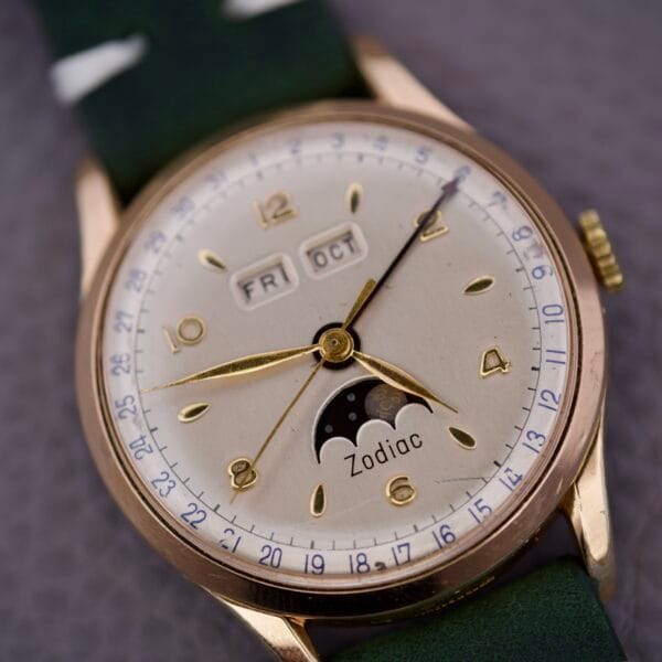 The Zodiac Triple Calendar Moonphase Cal. 12S wristwatch features a day, date, and moonphase display on a green strap, shown here in close-up.