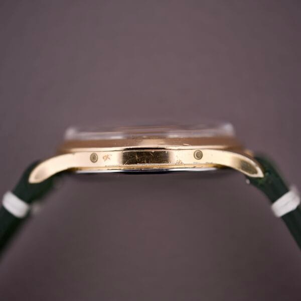 Close-up side view of the Zodiac Triple Calendar Moonphase Cal. 12S gold case with green straps, showcasing its Moonphase complication against a plain background.