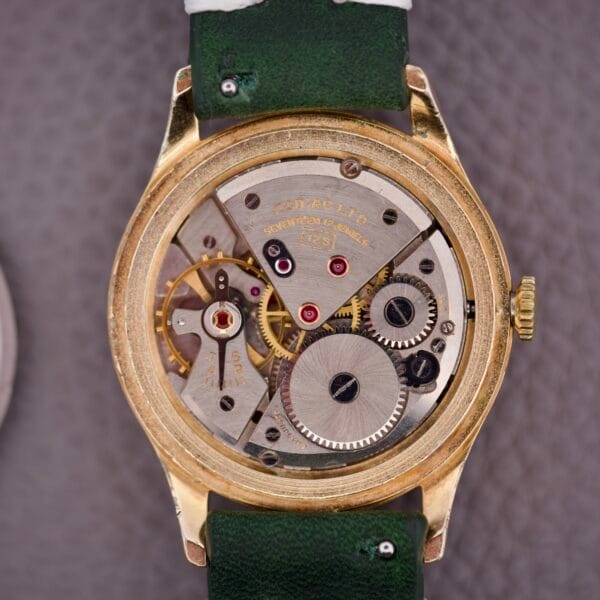 Close-up of the Zodiac Triple Calendar Moonphase Cal. 12S watch back, showing exposed gears and mechanical parts, with a green leather strap and classic triple calendar and moonphase complications.
