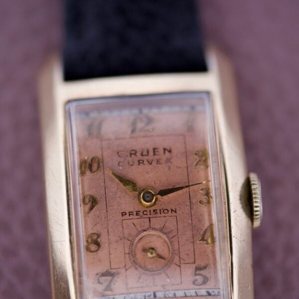 Close-up of the Gruen Curvex Precision Salmon Dial wristwatch, showcasing its rectangular gold case, leather strap, and elegant salmon-colored dial.