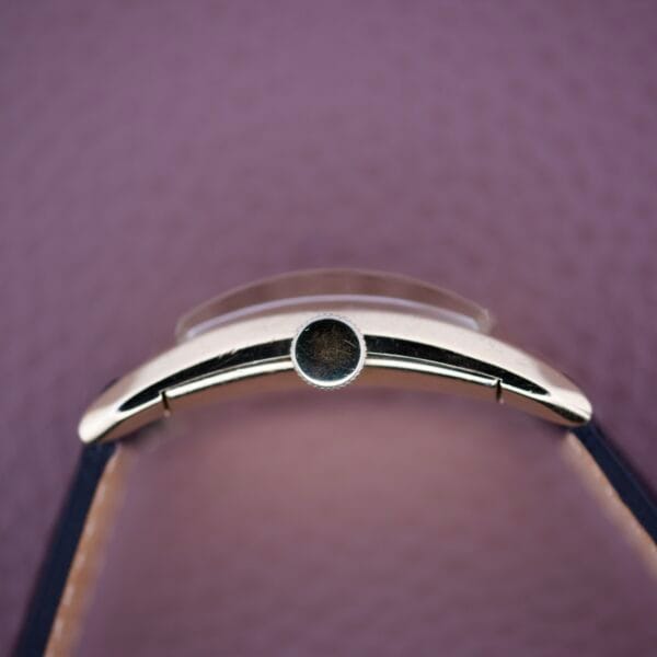 Side view of the Gruen Curvex Precision Salmon Dial wristwatch, featuring a round crown and fine detailing, set against a textured purple background.