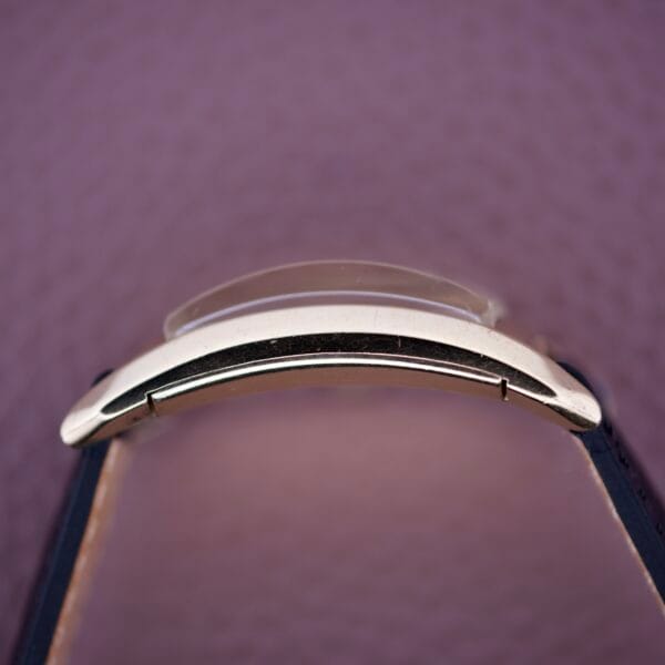 Close-up of a Gruen Curvex Precision Salmon Dial watch with a black strap, highlighting expert craftsmanship against a purple textured background.