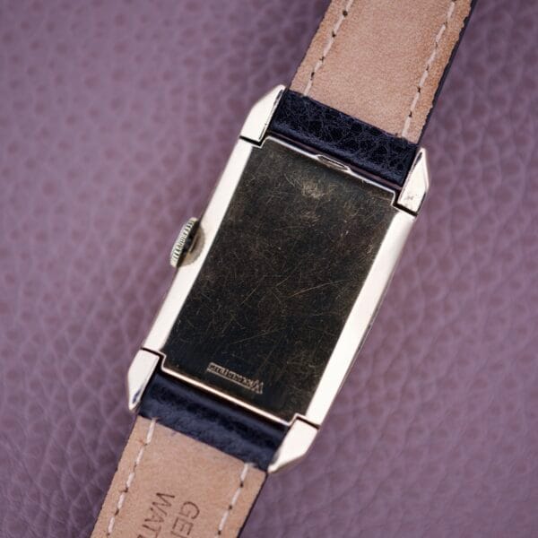 The Gruen Curvex Precision Salmon Dial watch features a gold rectangular case and leather strap, displayed from the back on a textured pink surface. Renowned for its classic design and dependable craftsmanship.