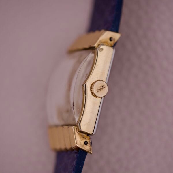 Close-up side view of a gold Gruen 21 Precision Tank USA Cal. 335 watch with a blue strap, highlighting its refined design.