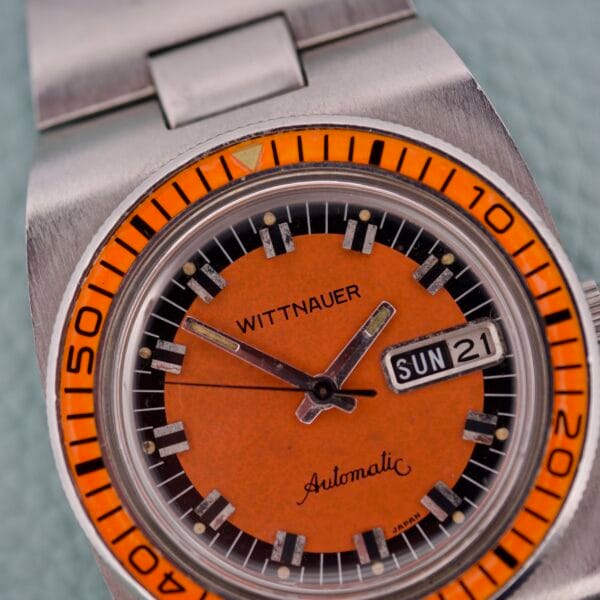 Close-up of a Wittnauer Diver Bakelite Bezel 1002-W100 automatic wristwatch featuring an orange dial and displaying the day and date as Sunday 21.