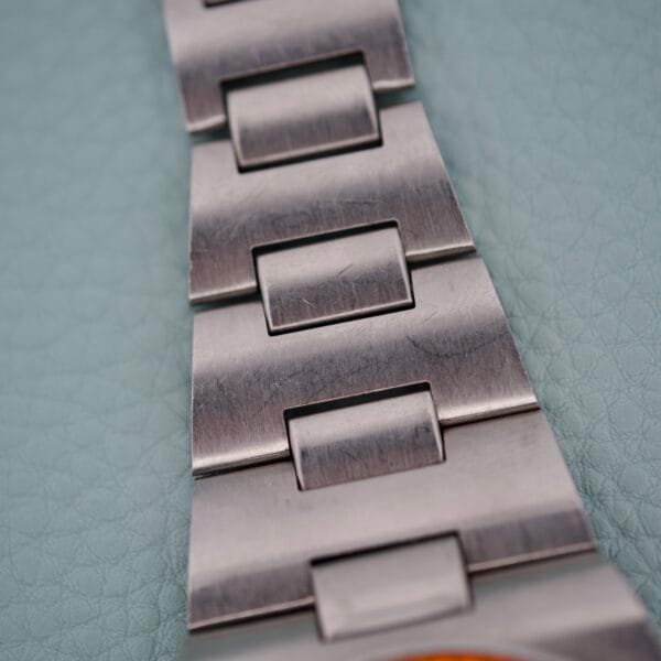 Close-up of a brushed metal watch bracelet on a light blue textured background, showcasing the refined style of the Wittnauer Diver Bakelite Bezel 1002-W100.