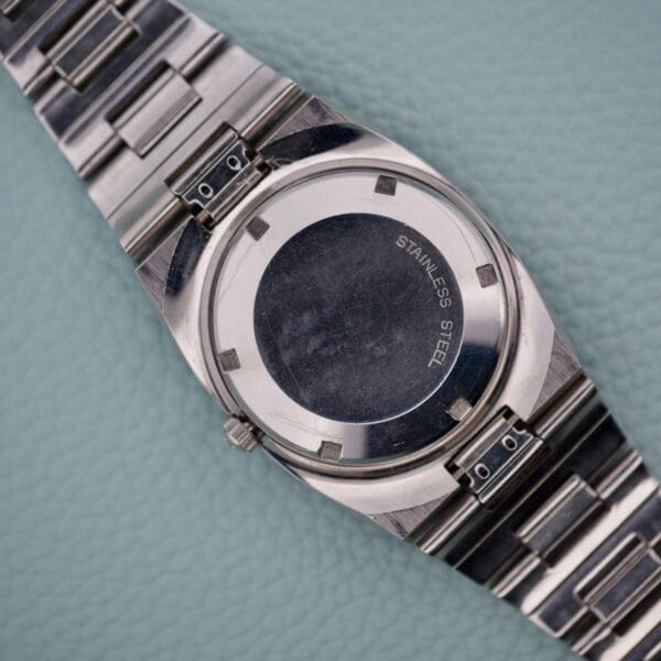 Back of a Wittnauer Diver Bakelite Bezel 1002-W100 stainless steel wristwatch with a metal band, displayed on a light blue textured surface.