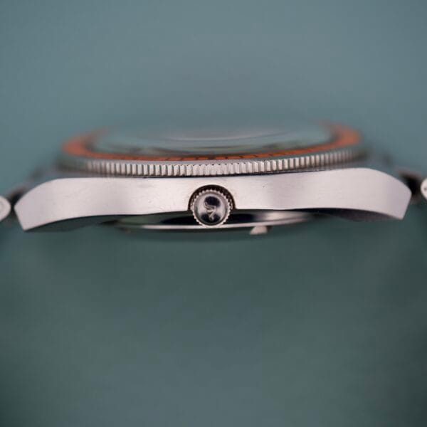 Side view of the Wittnauer Diver Bakelite Bezel 1002-W100 silver wristwatch case with a ridged Bakelite bezel and crown, set against a teal background.