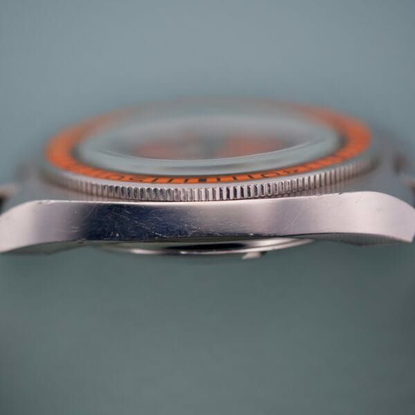 Close-up side view of a Wittnauer Diver Bakelite Bezel 1002-W100 wristwatch, showcasing its orange Bakelite bezel and metal case with visible scratches.