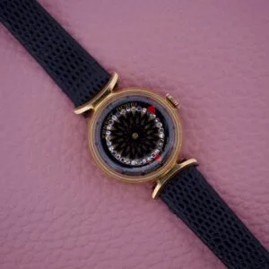 An Ernest Borel Kaleidoscope Cocktail 17 Jewels gold wristwatch with a black leather strap is displayed elegantly on a pink textured surface.