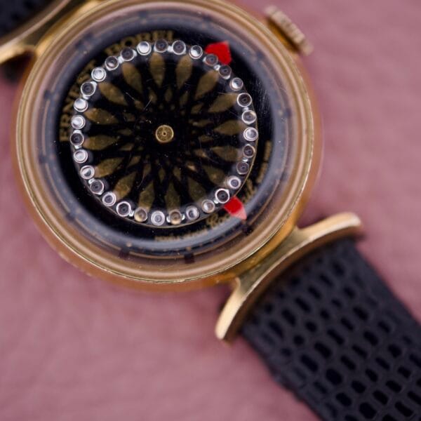 Close-up of the Ernest Borel Kaleidoscope Cocktail 17 Jewels wristwatch, featuring a circular black face, gold case, and black textured strap.