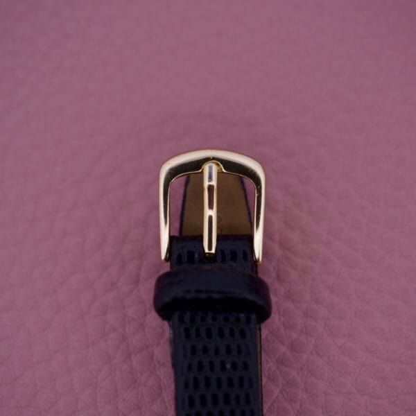 Black textured watch strap with a gold buckle, ideal for pairing with the Ernest Borel Kaleidoscope Cocktail 17 Jewels, shown on a mauve textured background.