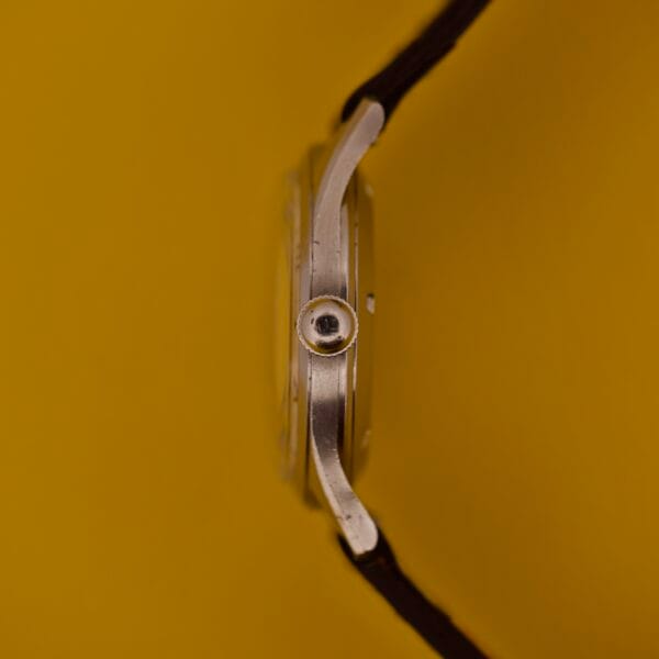 Side view of the Dom Watch Geneve 17 Jewels with a black strap and distinctive waffle dial, set against a solid yellow background.