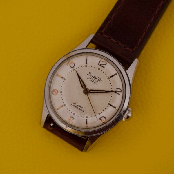 The Dom Watch Geneve 17 Jewels Waffle Dial, featuring a brown leather strap and classic waffle dial, is displayed on a bright yellow background.