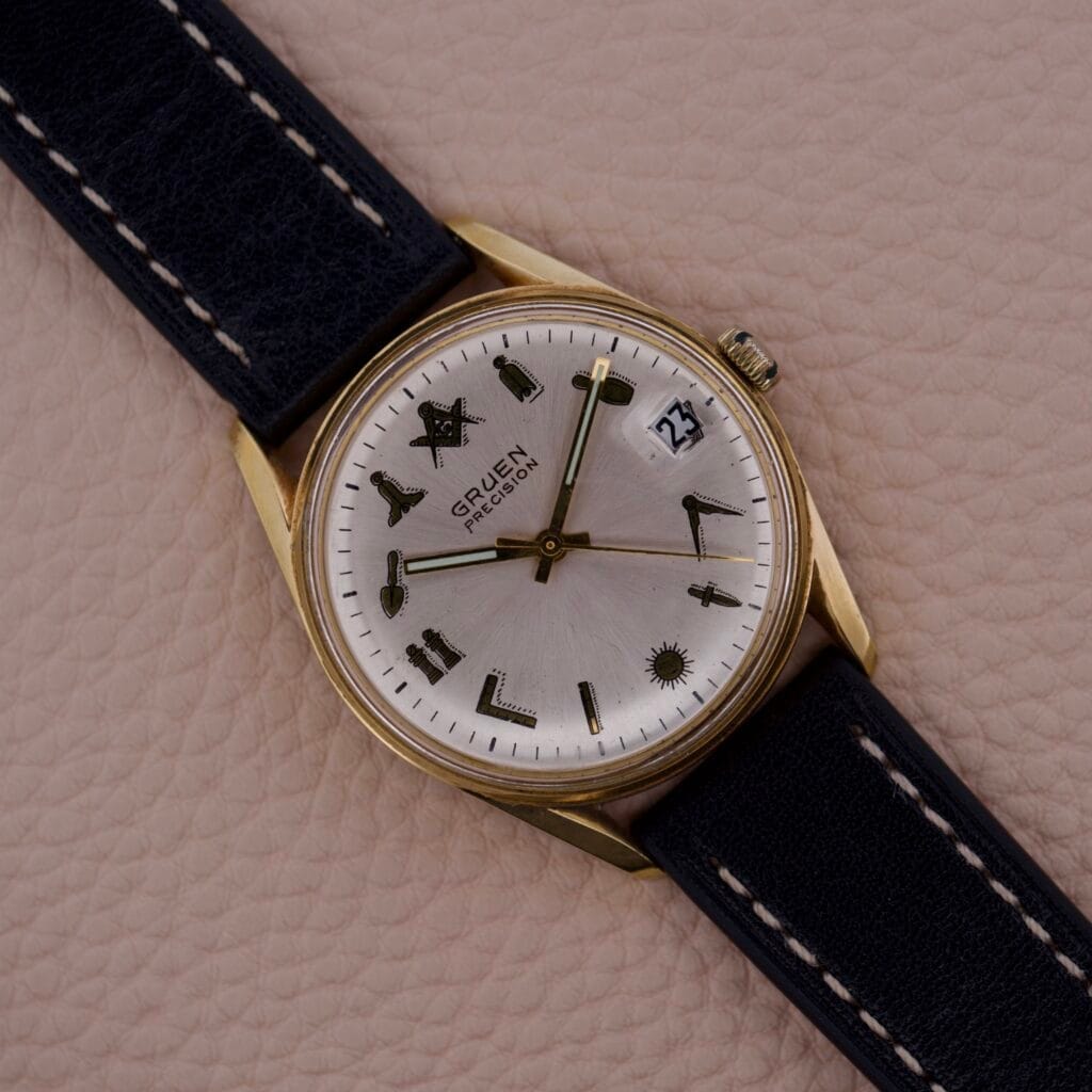 Gruen Precision 510 Date Masonic Dial watch featuring a gold case, black leather band, distinctive Masonic hour markers, and a date window at 3 oclock.