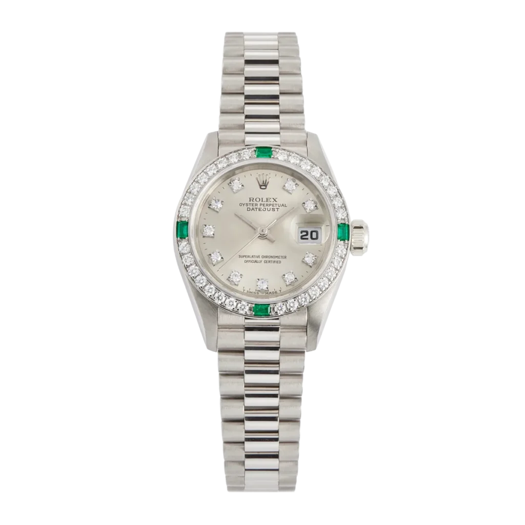 Silver Rolex Datejust 69079 watch with diamond and emerald accents, a date display, and a metallic link bracelet.