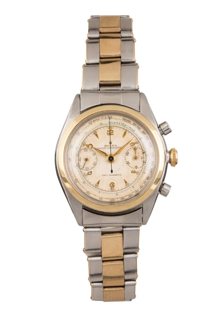 A vintage two-tone Rolex wristwatch with a round face, gold accents, chronograph features, and a metal link band.